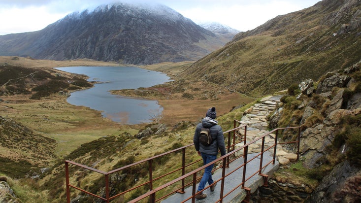 Walker on a footbridge overlooking Llyn Idwal in Cwm Idwal, Snowdonia, North Wales